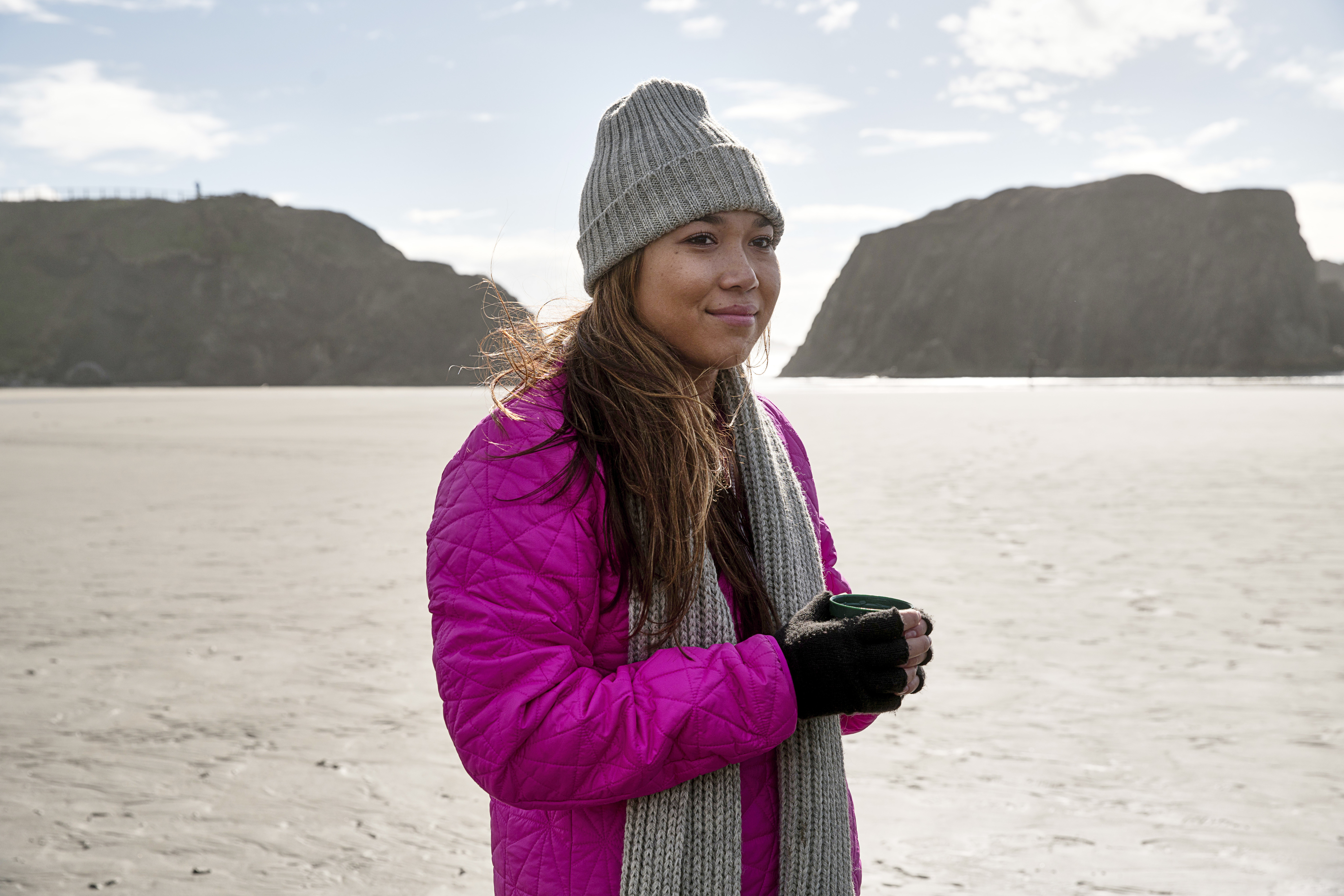 Woman in a pink coat standing on the beach in Bandon, Oregon.