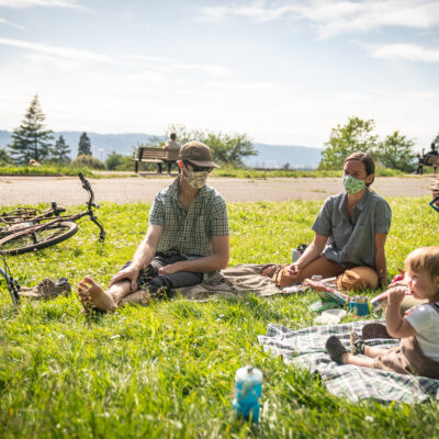 A group of masked people sitting outside at a picnic.