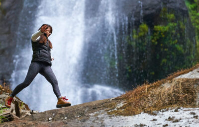 Woman walking across a log with a waterfall in the background.