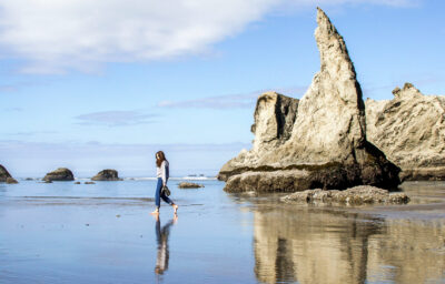 Photo of person walking along the ocean with beautiful rocks in background.