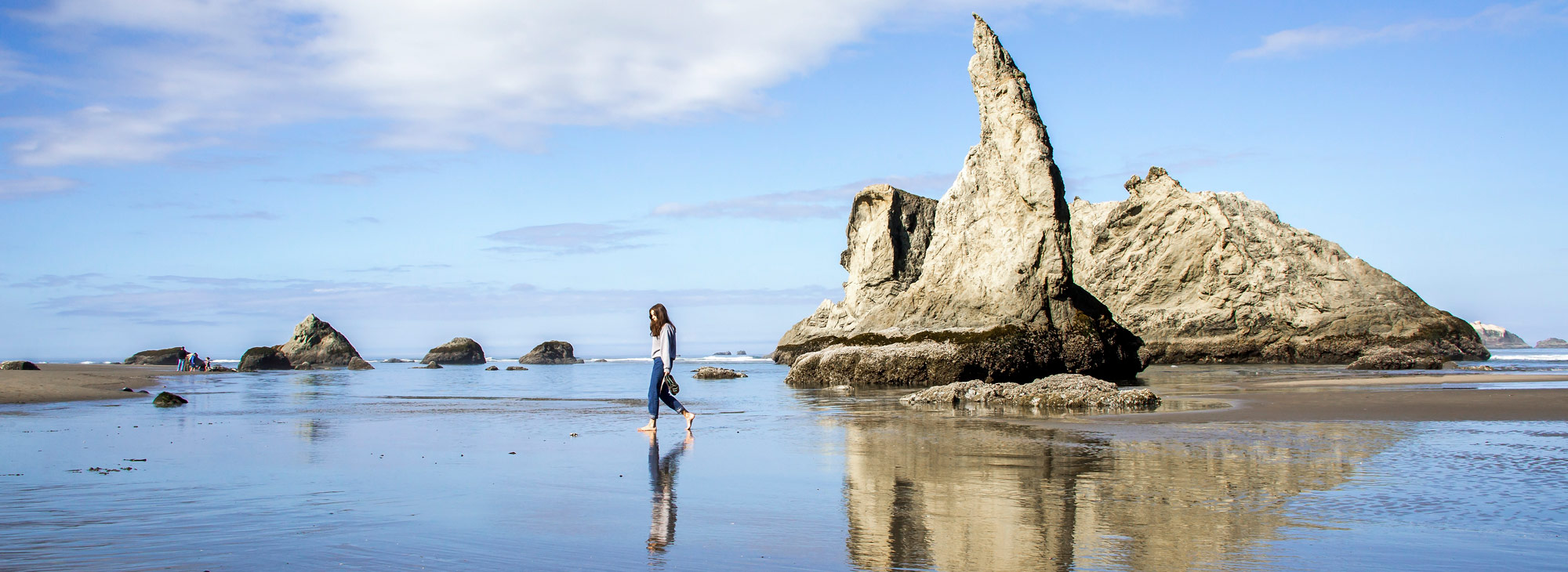 Photo of person walking along the ocean with beautiful rocks in background.