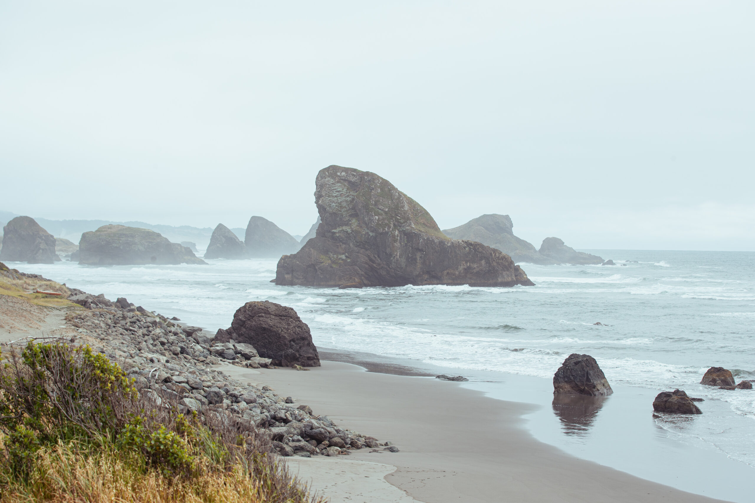 Rocky Oregon Coast shore with ocean and large rocks in the distance.