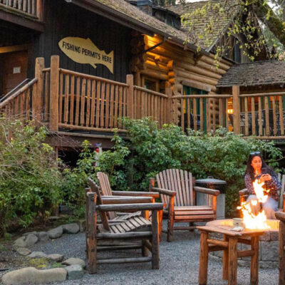 A rustic wooden lodge, "FISHING PIERNOTY RIVER," surrounded by trees, features guests seated around a fire pit. In the corner, the logo reads "NTT NATIONAL TRAVEL & TOURISM."