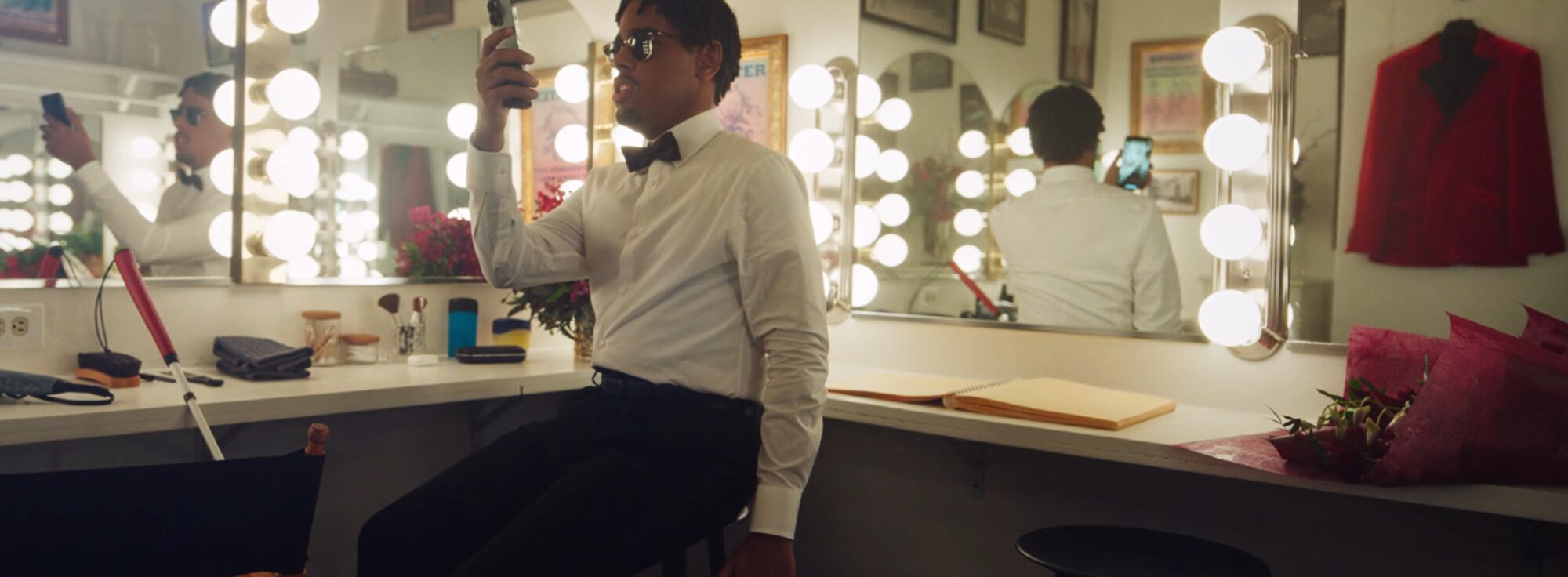 A man in a bow tie uses assistive technology on his phone to find items in a dressing room.
