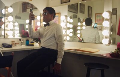 A man in a bow tie uses assistive technology on his phone to find items in a dressing room.