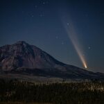 Image of Oregon Dark Sky with bright stars scattered across the sky, a rocky hill in the foreground and a large light beam aiming toward the sky.