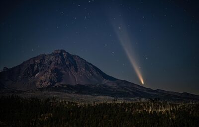 Image of Oregon Dark Sky with bright stars scattered across the sky, a rocky hill in the foreground and a large light beam aiming toward the sky.