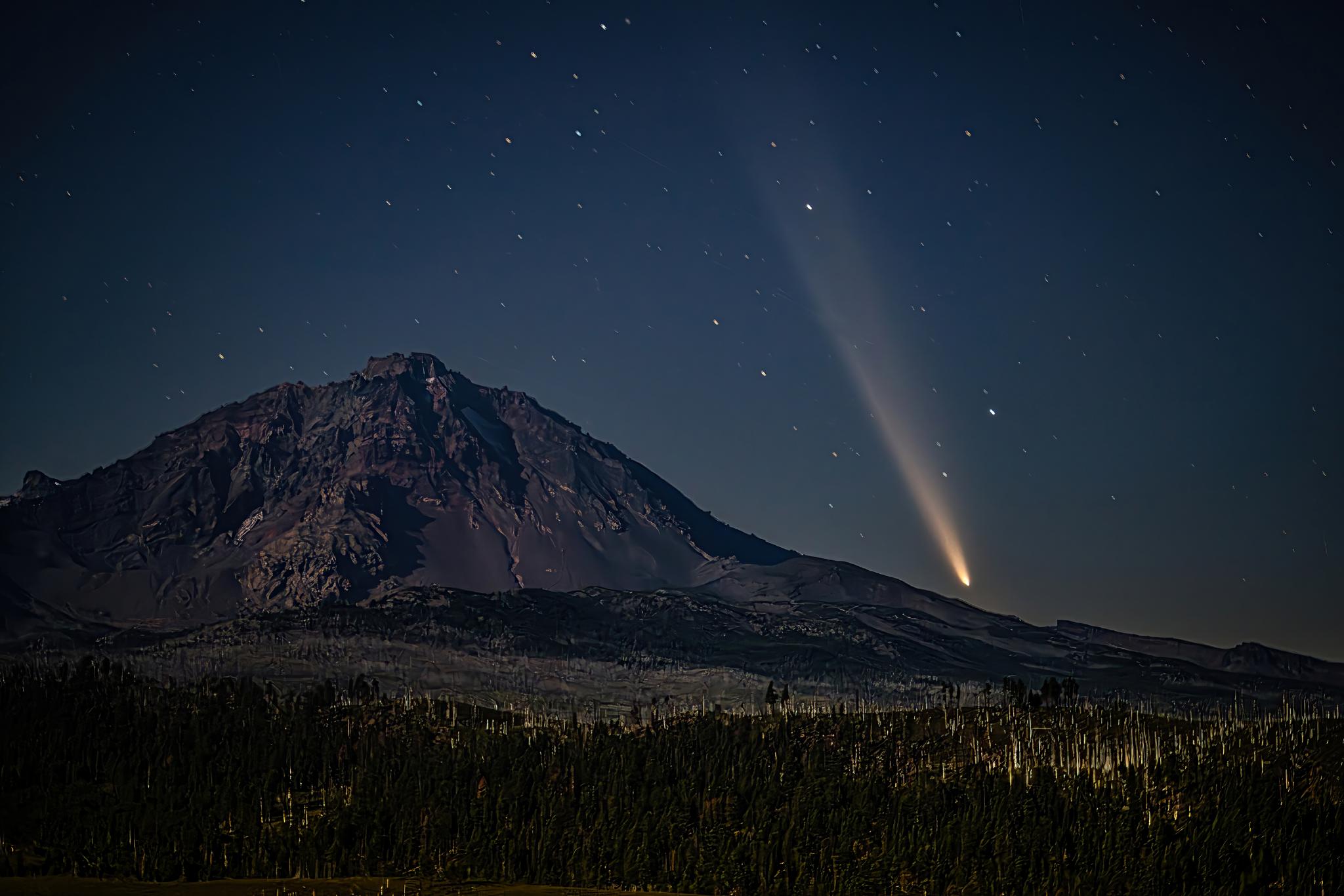 Image of Oregon Dark Sky with bright stars scattered across the sky, a rocky hill in the foreground and a large light beam aiming toward the sky.