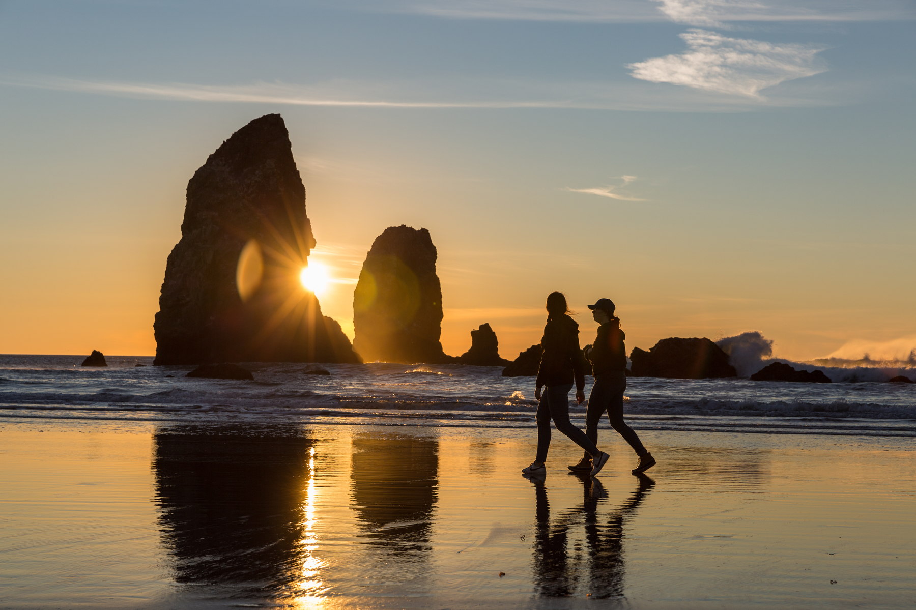 Two people walk across at Cannon Beach at sunet
