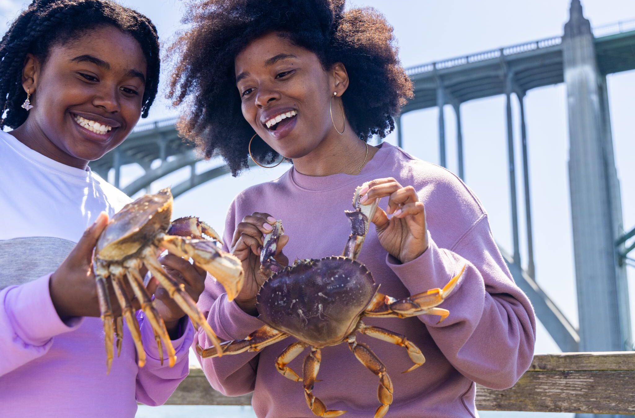 Two happy women hold up fresh-caught crabs.