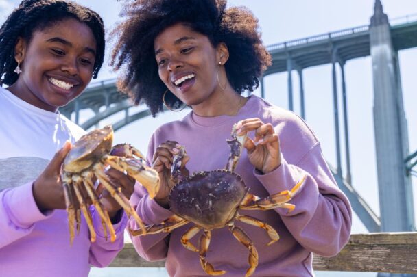 Two happy women hold up fresh-caught crabs.