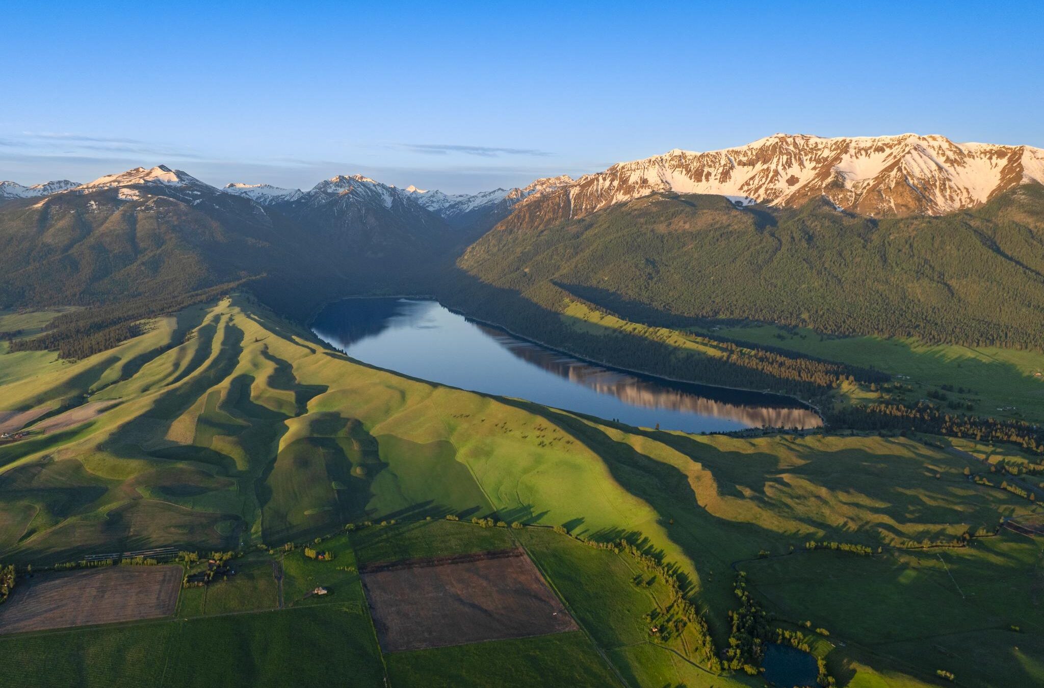 Sunrise over Wallowa Lake with green hills and snow capped mountains surrounding blue water