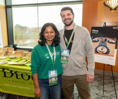 Two people standing side-by-side smiling in front of an exhibitor table at the Governor's Conference