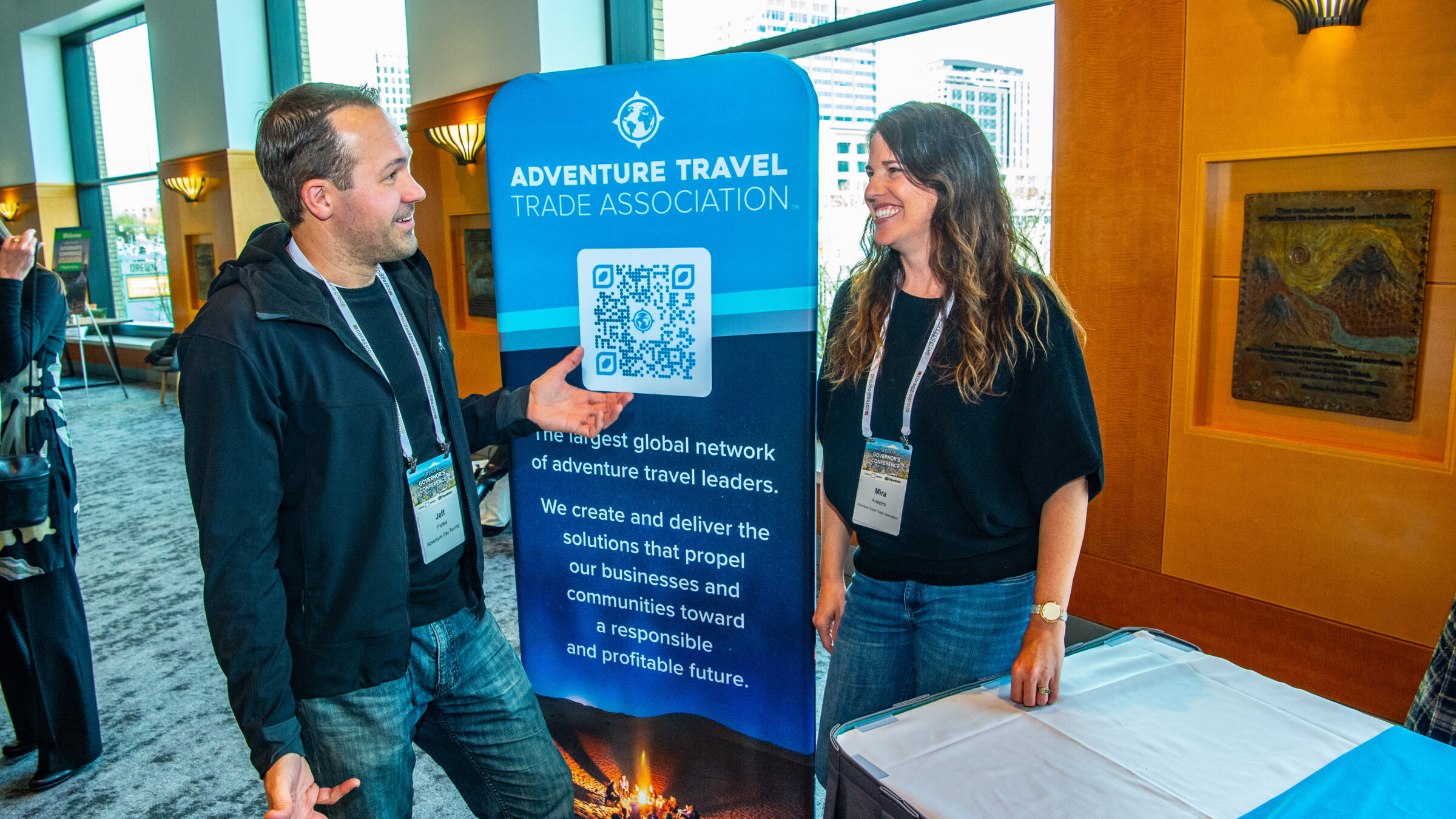 Two people standing near a blue banner at a conference exhibitor booth of happily conversing with one another