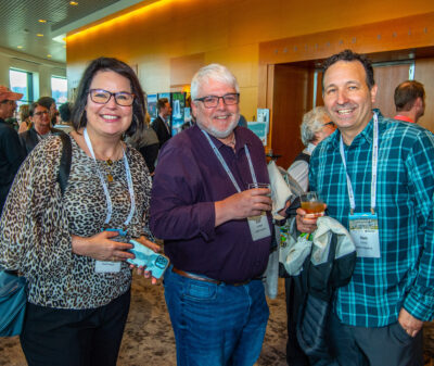 Three people standing side-by-side in an exhibitor hall with conference name badges